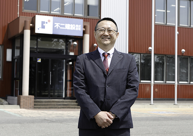 不二建設の社屋前で笑顔の職員